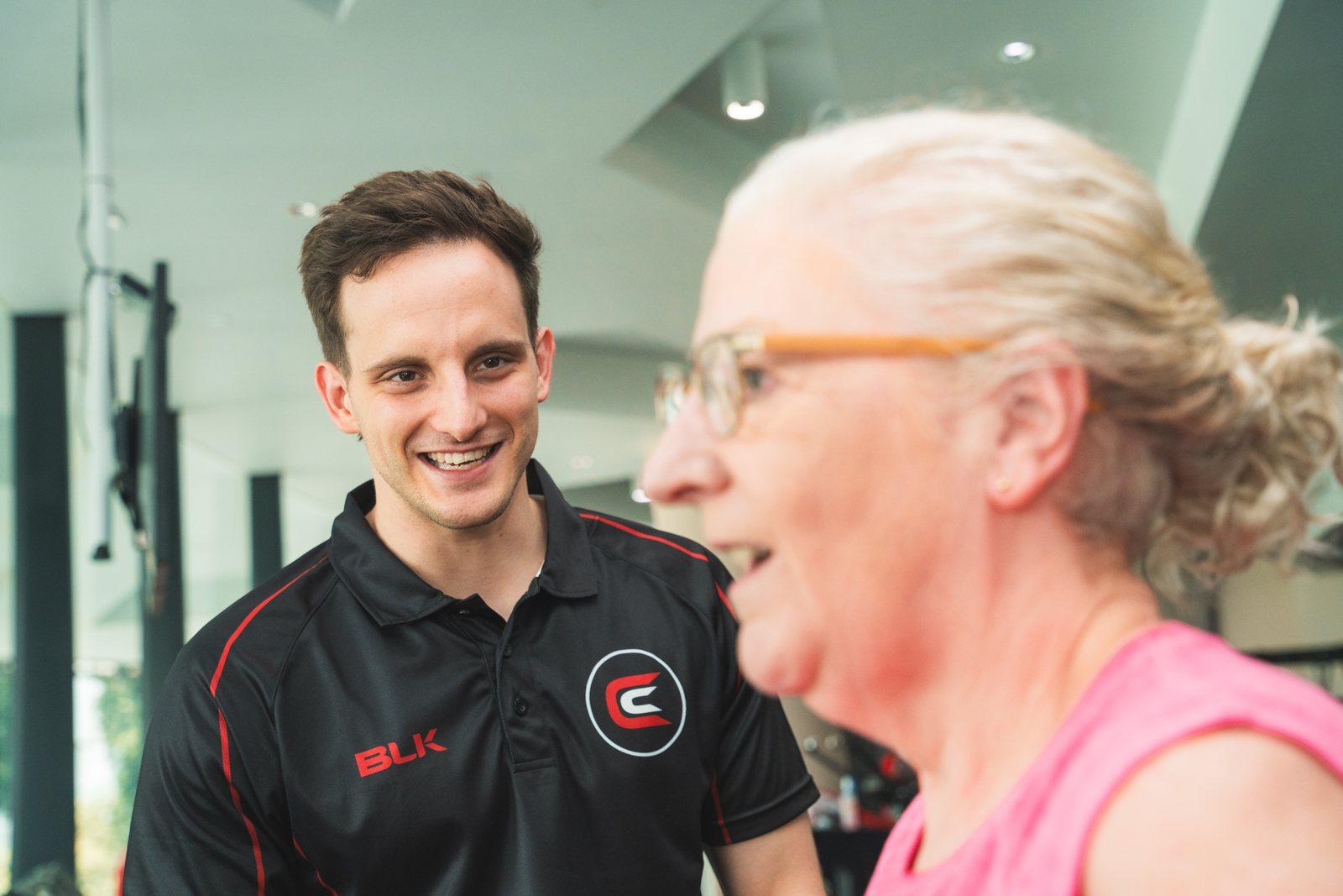 Nick Franich in a Catalyst polo, talking with an older client on the gym floor